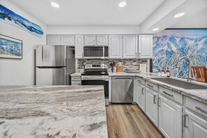 A modern kitchen with white cabinetry, stainless steel appliances, and a marble countertop.