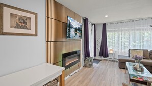 Ein modernes Wohnzimmer mit Kamin, einer Couch, einem Couchtisch und einem an der Wand montierten Fernseher.
