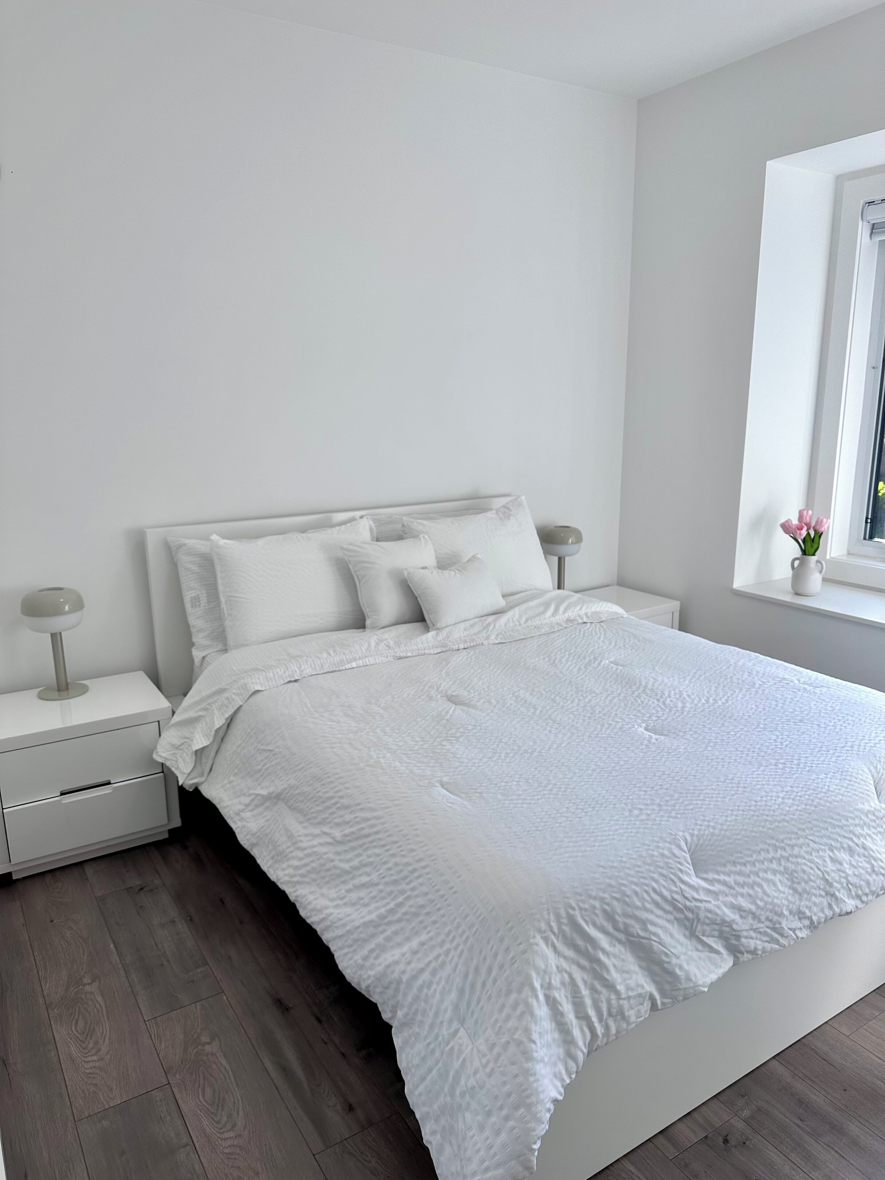 Ein schlicht eingerichtetes Schlafzimmer mit einem weißen Bett, Nachttischen und einem Fenster mit Aussicht.. YVR Stay - Vancouver YVR