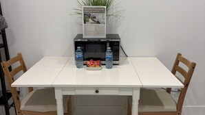 A white table with a microwave, two water bottles, and a small snack bowl. - YVR Stay - Vancouver YVR (Richmond)
