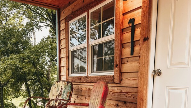 A wooden porch with two rocking chairs and a door with a number 1 sign. - The Cabins at Bent Pine Ranch ~ Cabin #1 (Locust Grove)