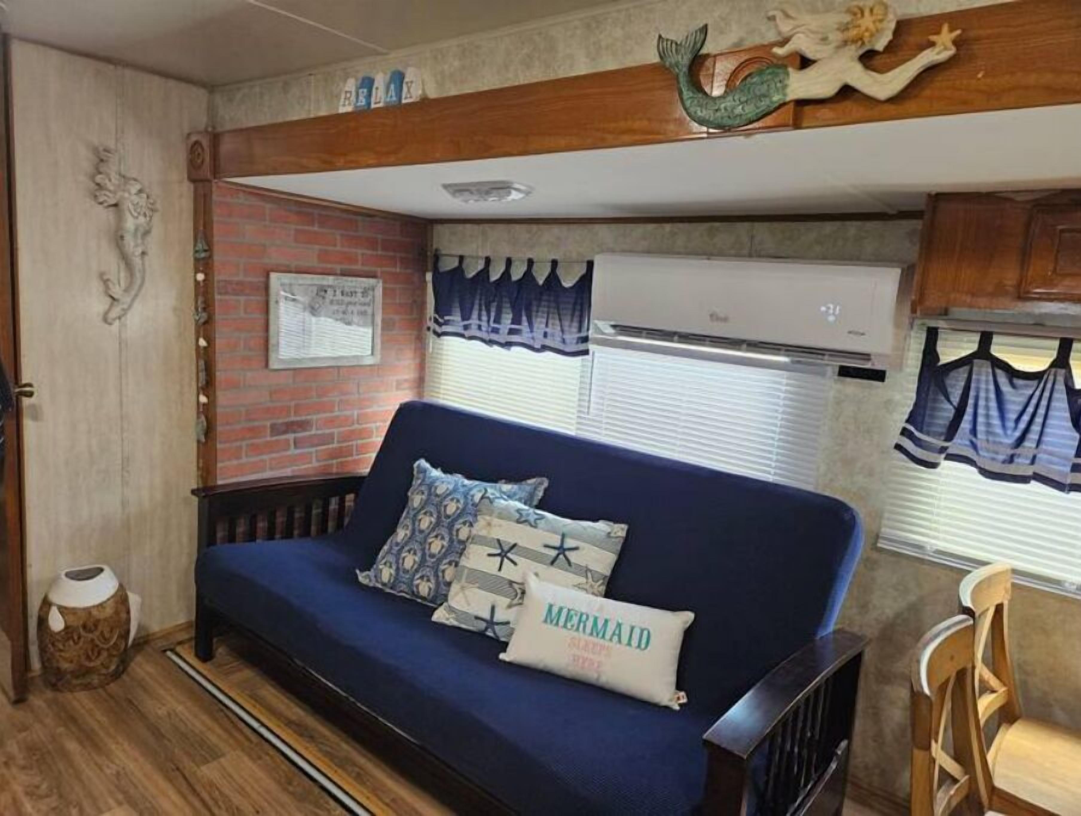 Interior aconchegante de uma motorhome, com um sofá azul, almofadas decorativas, um armário de madeira e uma parede de tijolos.