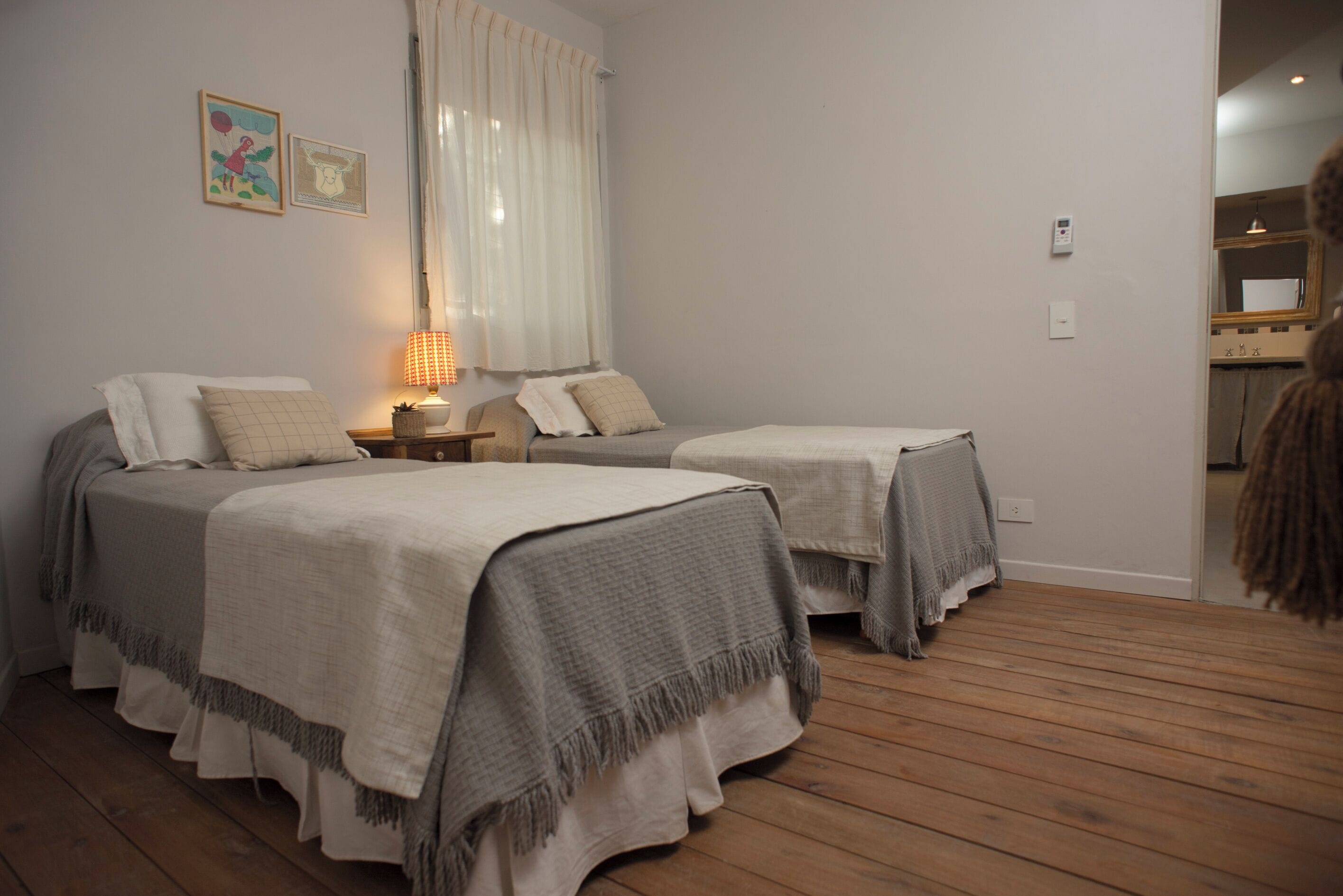 A room with two beds, a bedside table with a lamp, and a window with curtains.