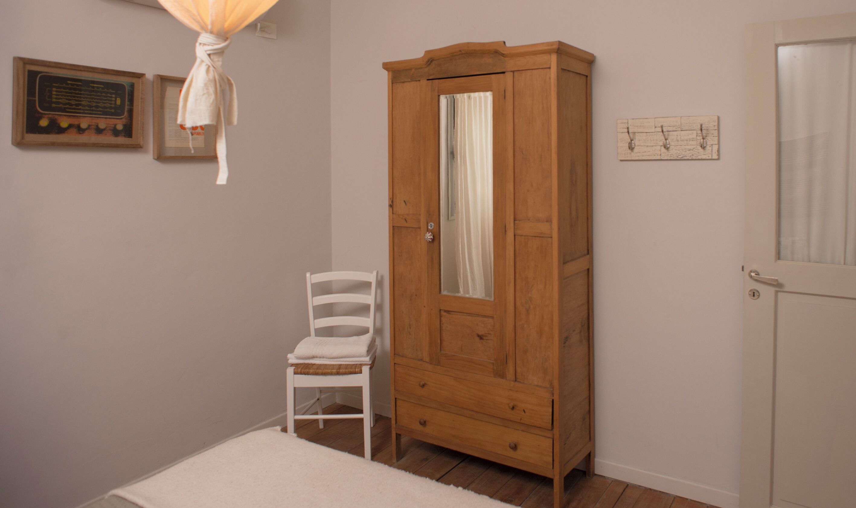 Een kamer met een houten garderobe, een witte stoel en een klein vloerkleed.