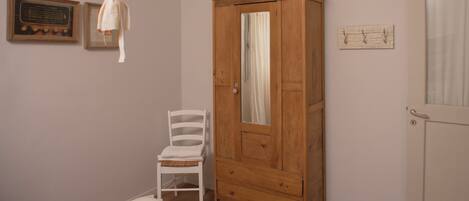 Een kamer met een houten garderobe, een witte stoel en een klein vloerkleed.