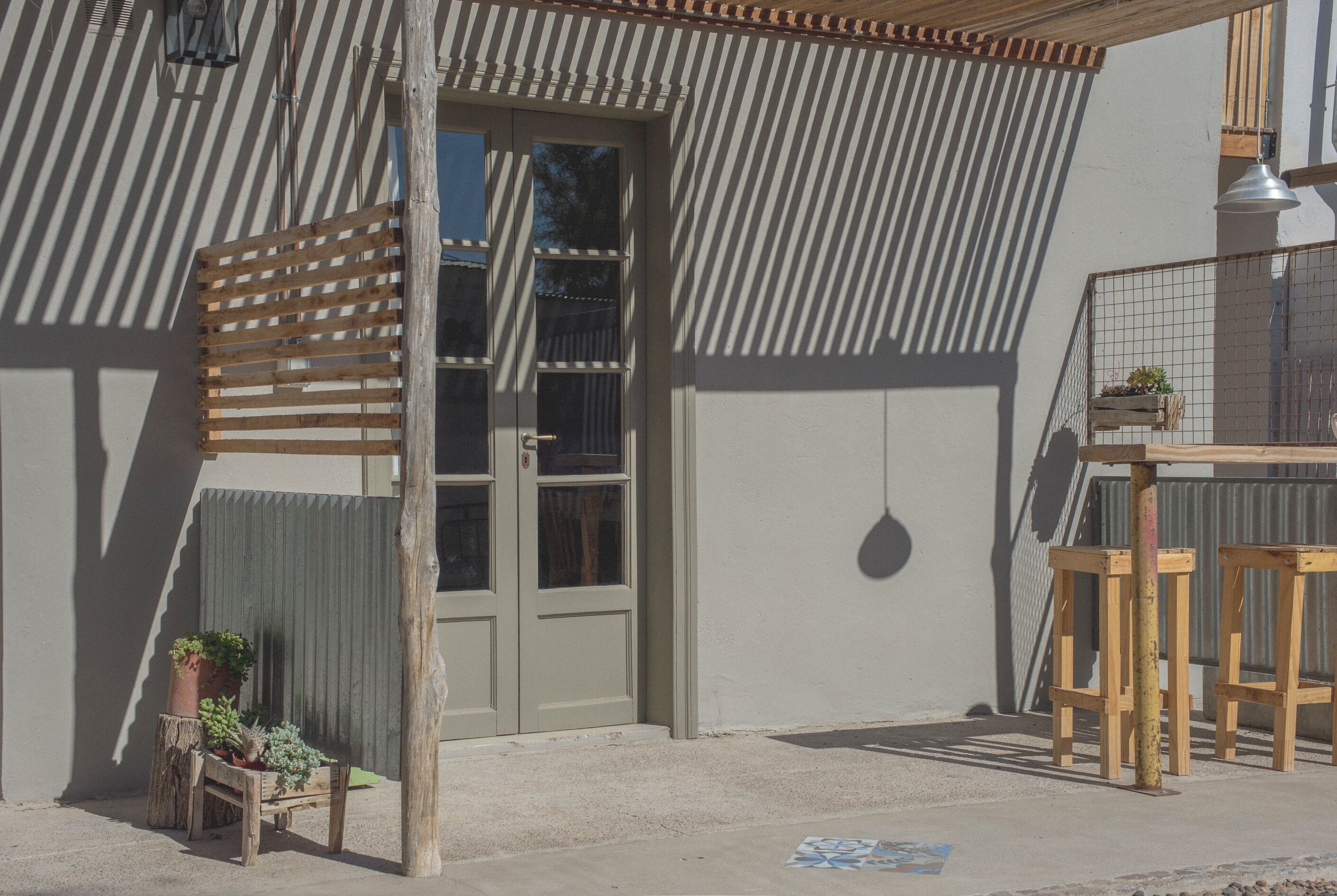 A building with a wooden slatted awning, a door, and a small wooden bench with potted plants.