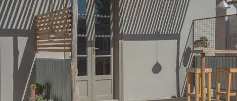 A building with a wooden slatted awning, a door, and a small wooden bench with potted plants.