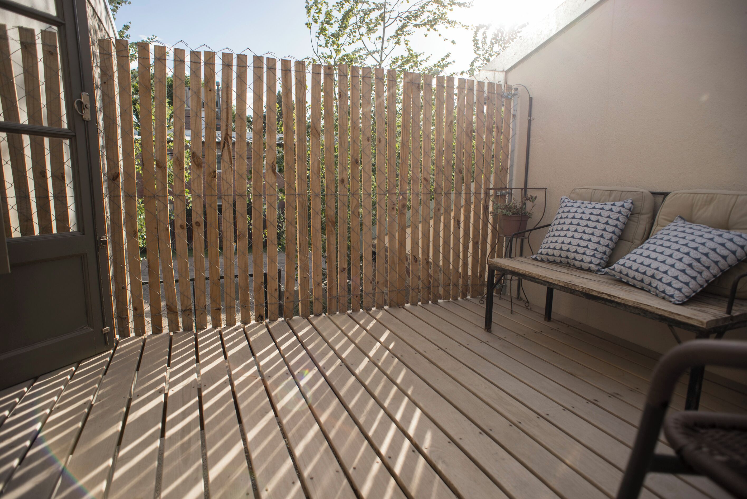 A wooden deck with a fence, a bench, and a door.