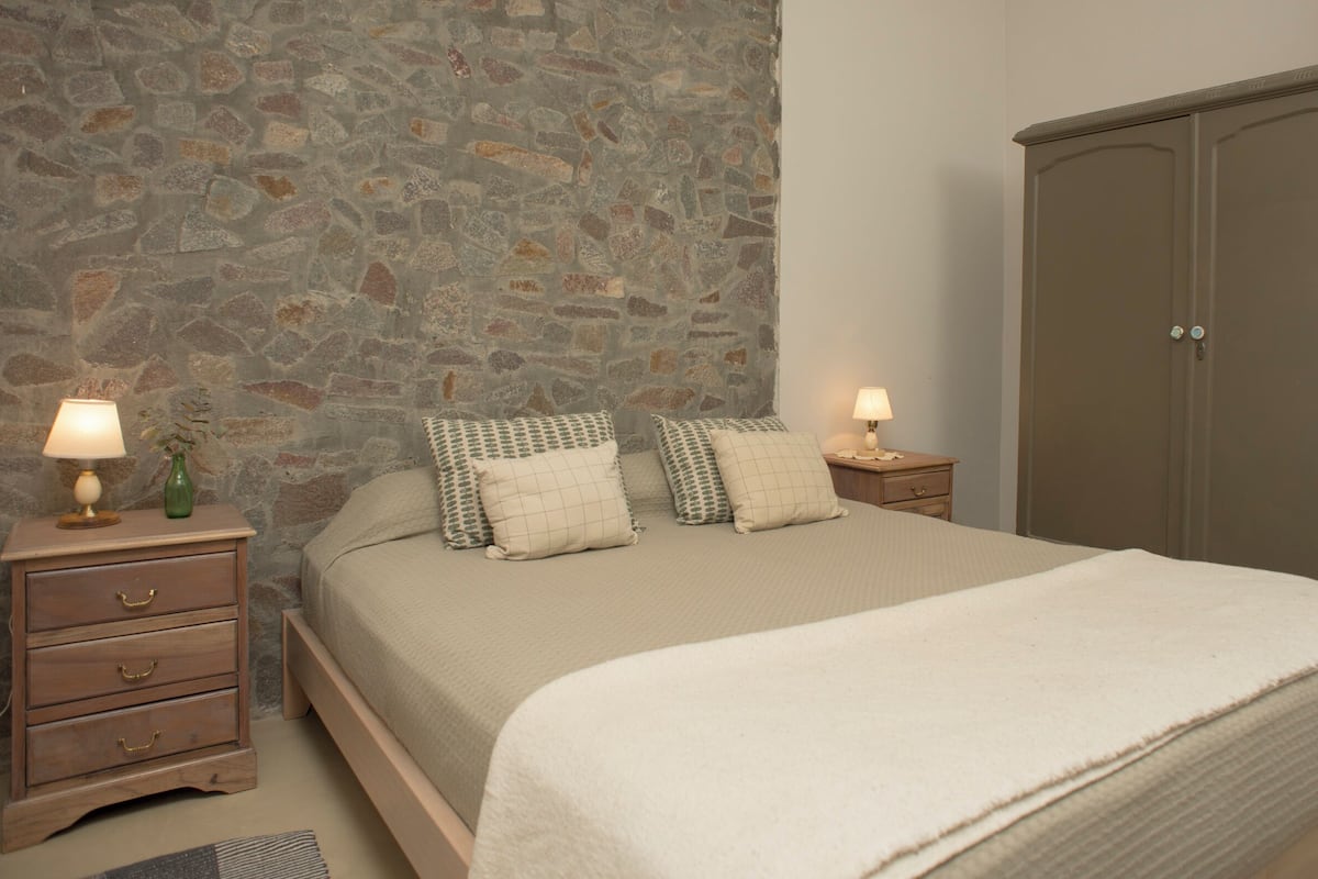 Ein Schlafzimmer mit Steinsturz, einem hölzernen Bett mit beiger Bettdecke, zwei Nachttischen mit Lampen und einem Holzschrank.
