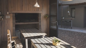 An outdoor wooden deck with a built-in grill, wooden benches, and hanging pendant lights. - El Poblado (Puerto Madryn)