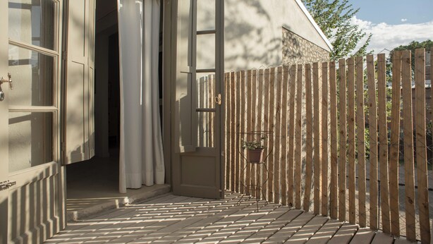 A wooden deck with a metal gate, a potted plant, and a door leading to a building. - El Poblado (Puerto Madryn)
