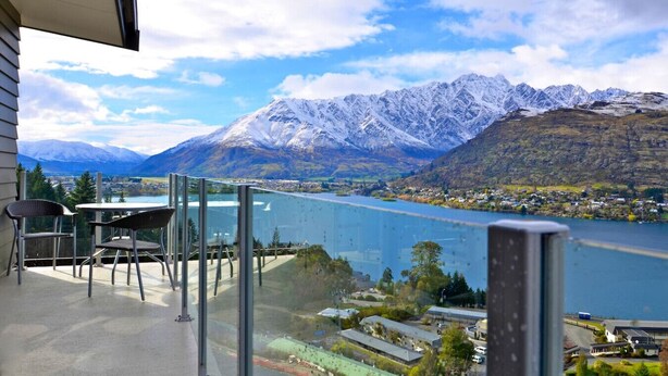 Ein Balkon mit Tisch und Stühlen, mit Blick auf einen See und schneebedeckte Berge.
