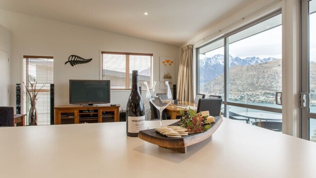 Un salon moderne doté d’une grande fenêtre, d’un téléviseur à écran plat, d’une bouteille de vin et d’une table à manger agrémentée d’un centre de table.