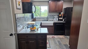 A modern kitchen with dark wood cabinets, a black refrigerator, and a glass island with a bowl of fruit.