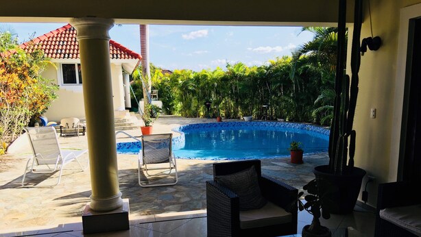 A poolside area with a tiled floor, lounge chairs, a wicker sofa, and a glass table. - DREAM VACATION HOME (Sosúa)