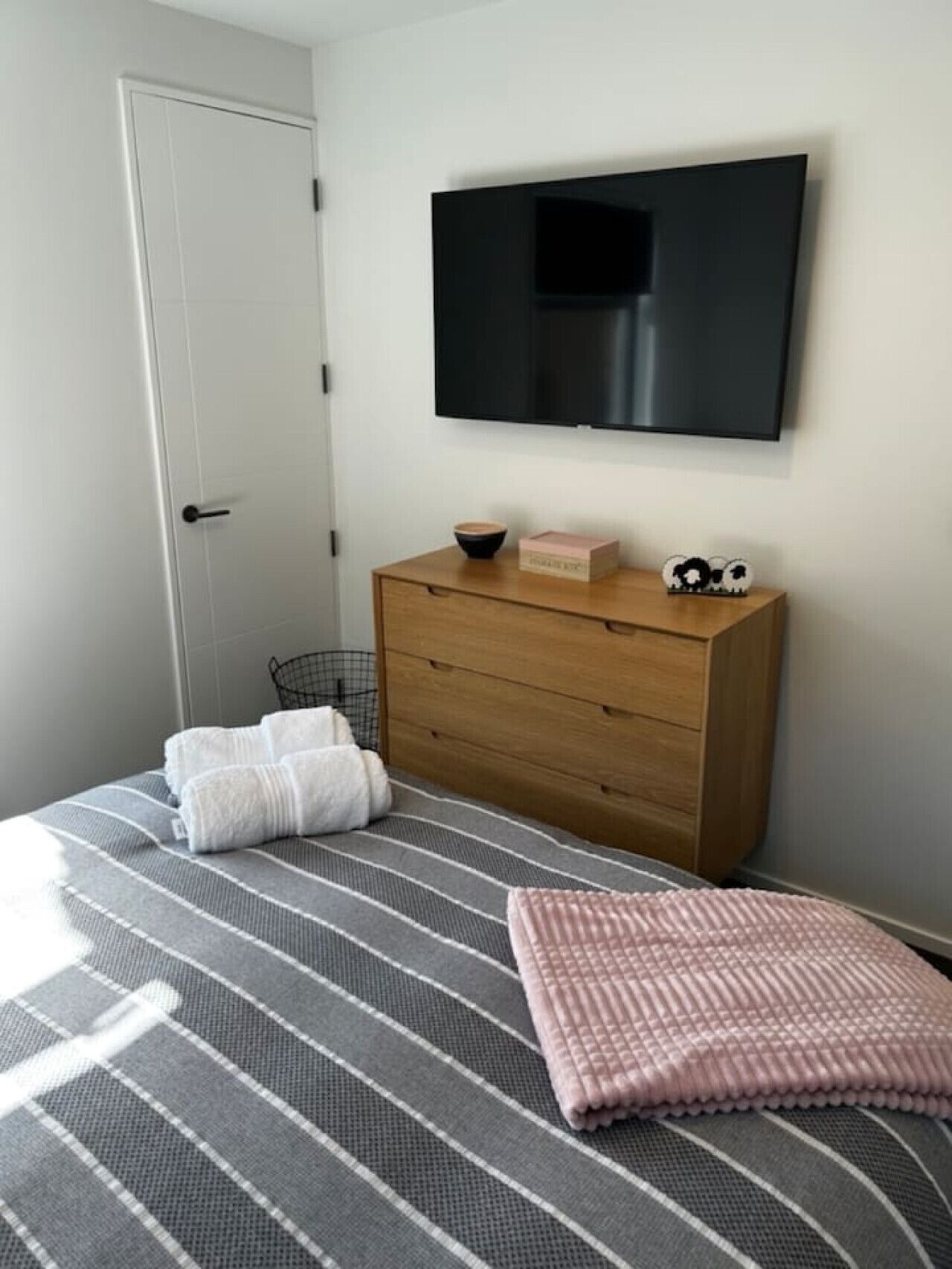 A bedroom with a bed, a wooden dresser, a television, and a door.