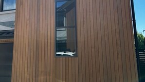 Un bâtiment moderne avec un revêtement extérieur en bois disposé verticalement et une fenêtre centrale.