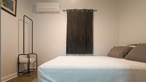 Un dormitorio con cama, ventilador de techo, cortina oscura, aire acondicionado de pared y un perchero con toallas.