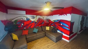 Una habitación con un sofá seccional marrón, un ventilador de techo y un vibrante mural abstracto en la pared.