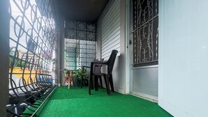 Un espacio exterior techado con piso verde artificial, barandales metálicos y una silla.