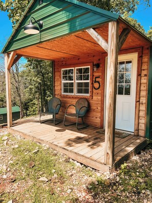 Una cabaña de madera con un porche, dos sillas y una puerta con el número 5.