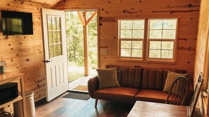 A cozy cabin interior with a wooden ceiling, a sofa, a table, and a TV mounted on the wall.