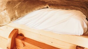 A wooden cabin interior with a single bed, a ceiling light, and a sloped roof.