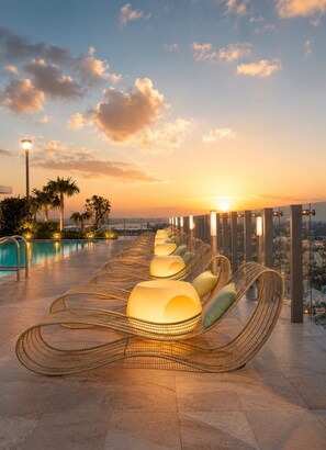 Un espace piscine sur le toit, avec des chaises longues et une vue imprenable sur le coucher de soleil.