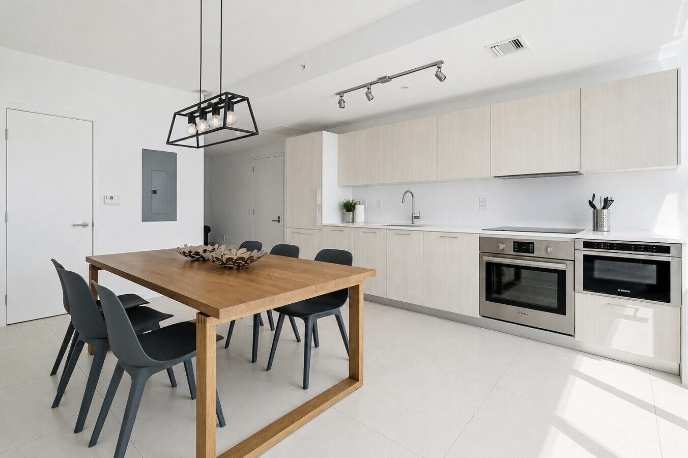 Une cuisine moderne avec une table à manger en bois, des chaises noires et des appareils électroménagers en acier inoxydable.