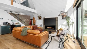 A modern living room with a large sofa, a fireplace, and a dining area with a kitchen in the background.