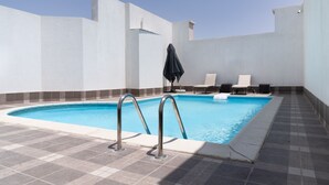 Una piscina amb un solàrium enrajolat, dues gandules i un parasol negre.