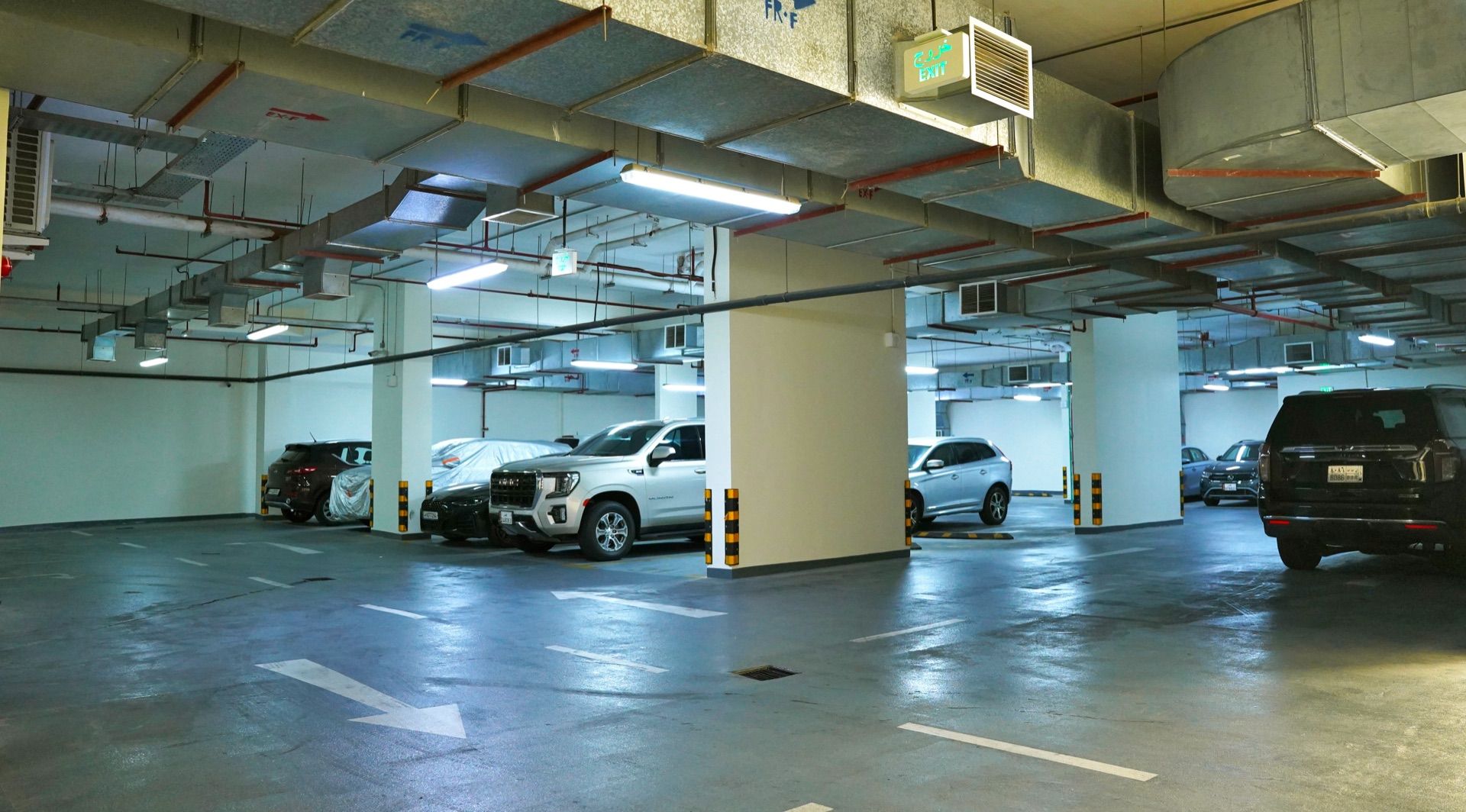 An underground parking garage with multiple levels, concrete pillars, and directional arrows on the floor.