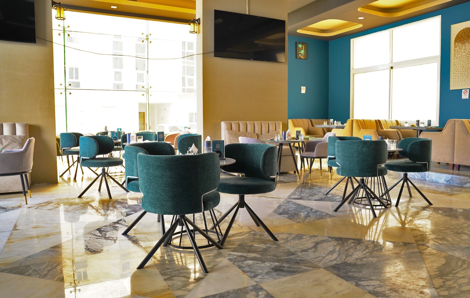 A spacious lobby with a marble floor, teal chairs, and a seating area with sofas and tables.