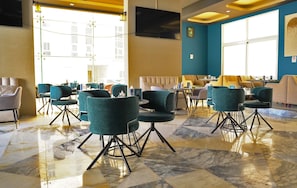 Een ruime lobby met een marmeren vloer, teal stoelen en een zithoek met banken en tafels.