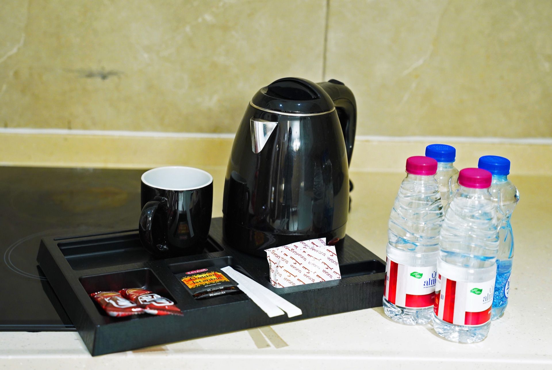 A breakfast tray with a black coffee pot, a white mug, and four water bottles with red and blue caps.