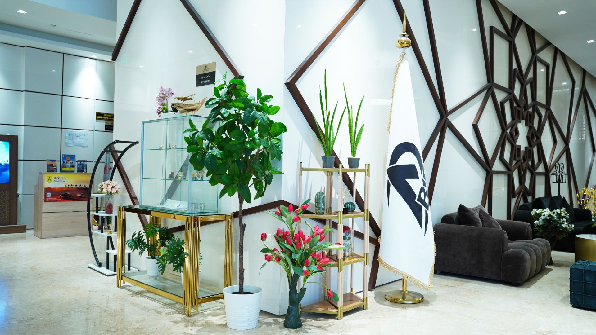 A modern lobby with a glass display, potted plants, a seating area, and a geometric wall design.