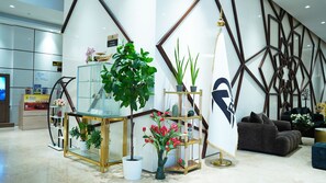 A modern lobby with a glass display, potted plants, a seating area, and a geometric wall design.
