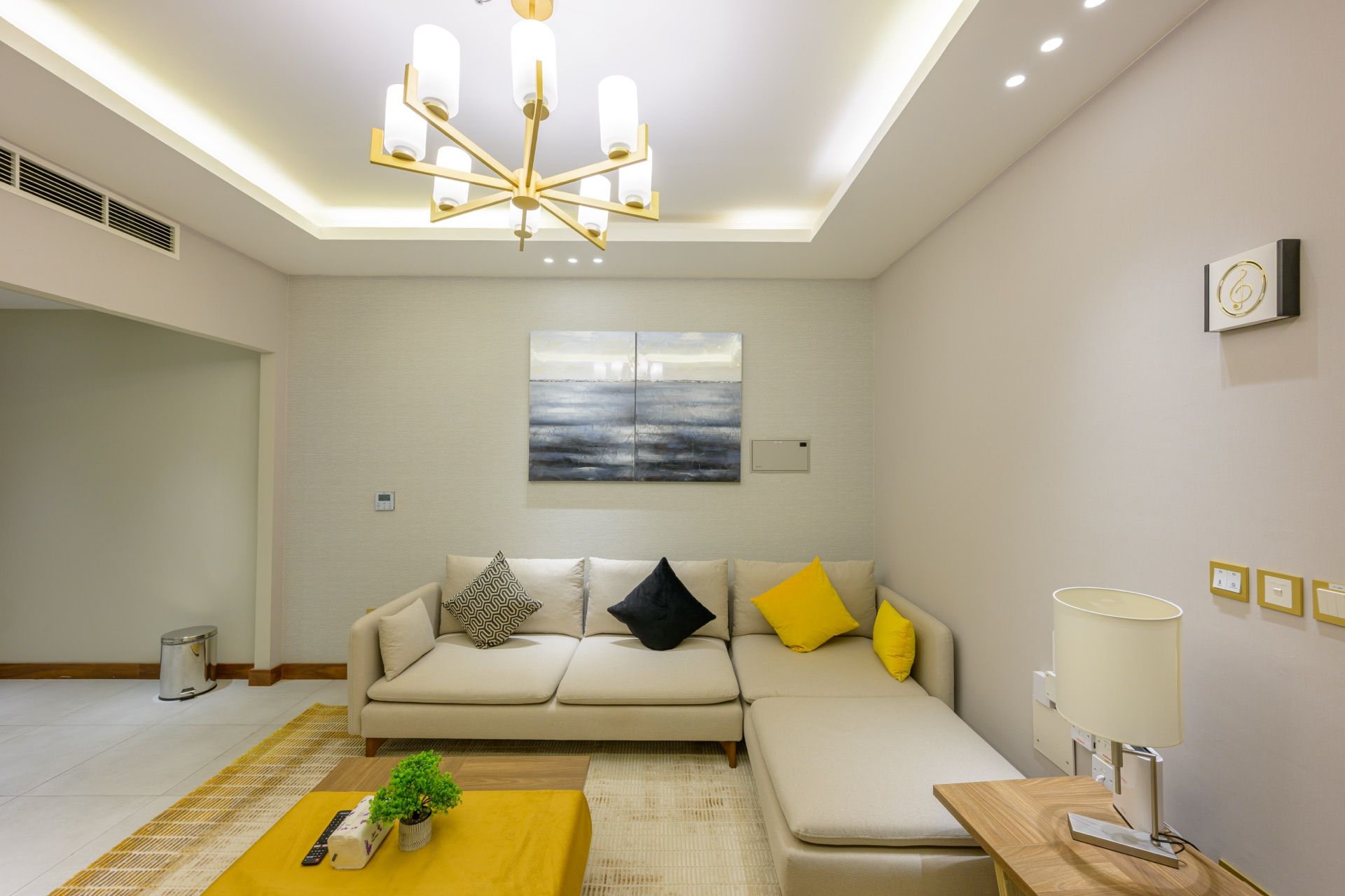 A modern living room with a sectional sofa, a small table, a lamp, and a ceiling light fixture.