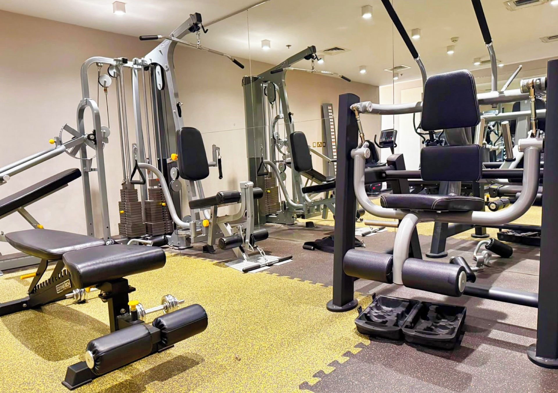 A gym with various exercise machines, benches, and a yellow rubber mat floor.