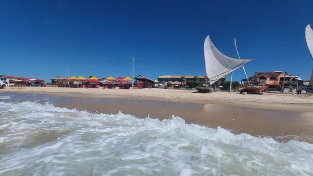 Una playa con olas, sombrillas y edificios al fondo.