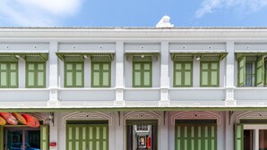 Ein zweistöckiges Gebäude mit grünen Fensterläden und weißen Wänden, mit einem zentralen Eingang und einem dekorativen Bogen.
