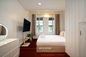 A hotel room with a bed, a TV, a desk, and a window with curtains.