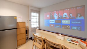 Eine moderne Küche mit Kühlschrank, Holzschränken, einem Esstisch mit Stühlen und einem großen Bildschirm, der verschiedene Streaming-Dienste anzeigt.