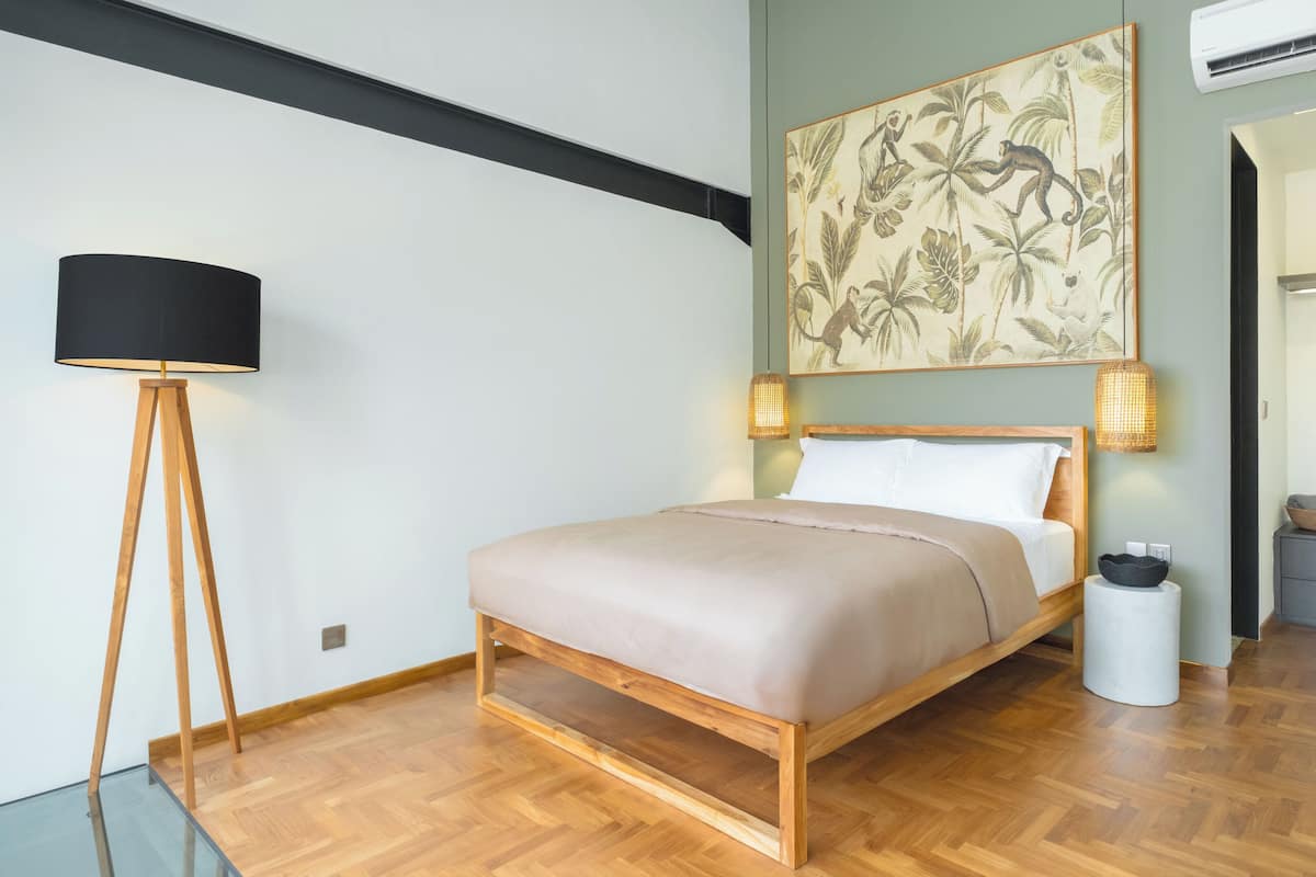 A modern bedroom with a wooden bed, two bedside lamps, a floor lamp, a wall-mounted air conditioner, and a small side table with a basket.