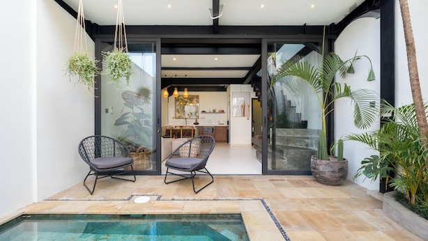 Un patio exterior moderno con piscina, dos sillas de mimbre y plantas en macetas.