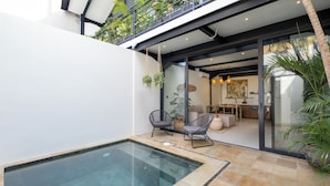 Una casa moderna con un porche de vidrio, una piscina y un comedor con una cocina visible a través de las puertas de cristal.