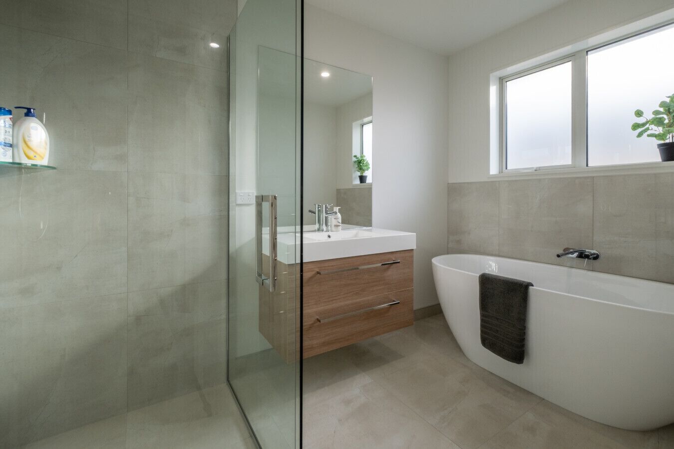 A modern bathroom with a glass shower enclosure, a wooden vanity with a sink, and a freestanding bathtub.