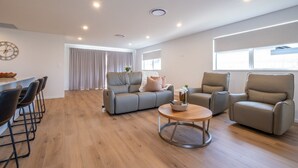 A spacious living area with a grey sofa, two armchairs, a coffee table, and a dining area with bar stools.
