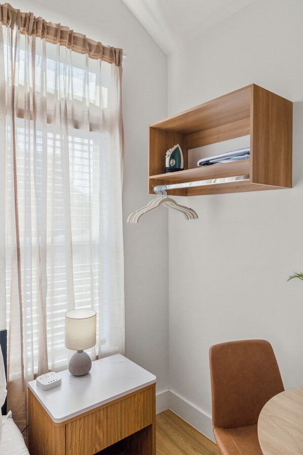A modern room with a wooden nightstand, a lamp, a chair, and a shelf with books and a small house model.