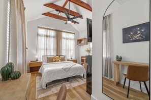A bedroom with a bed, bedside table, lamp, and a desk with a chair.